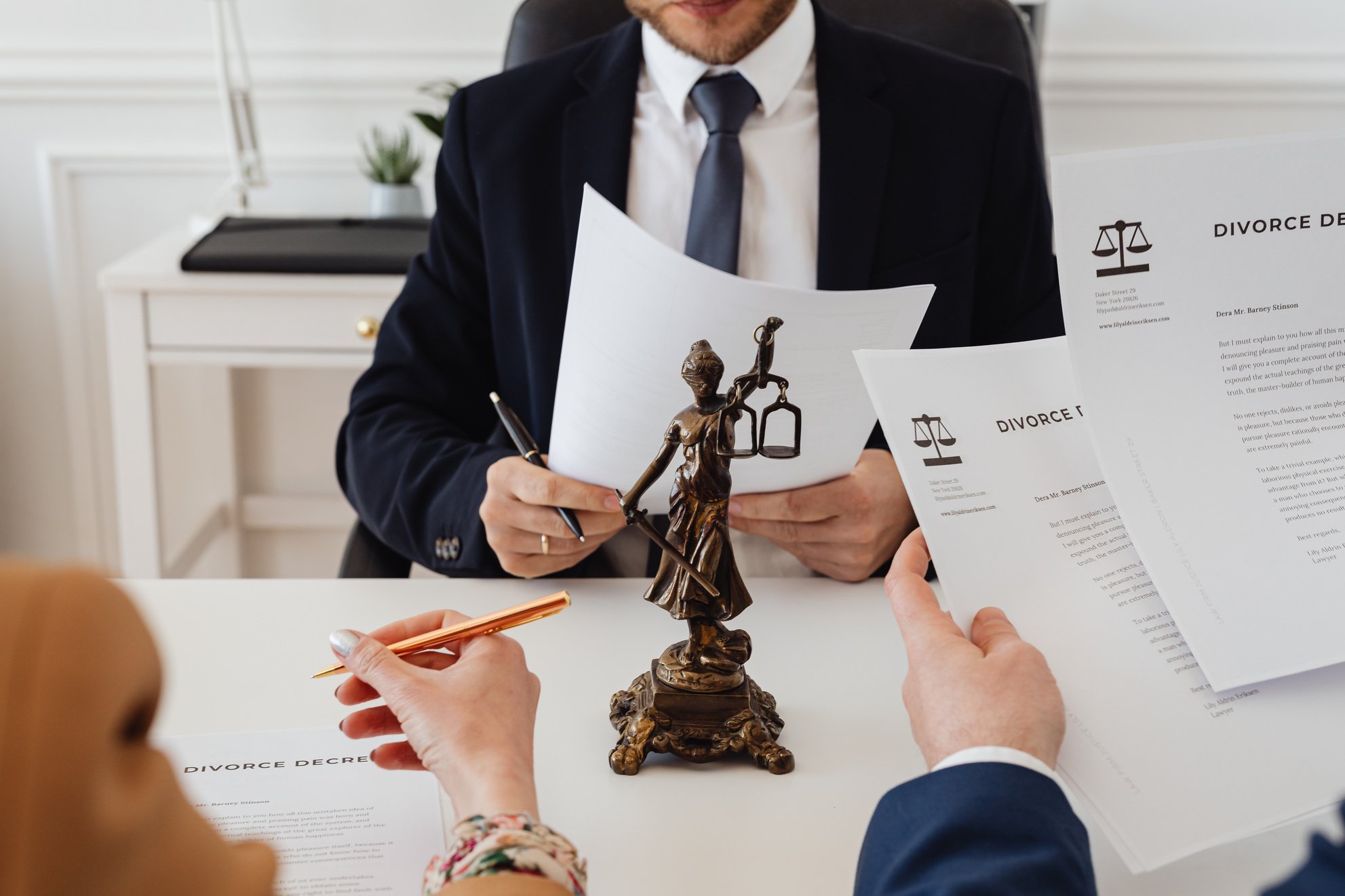 two people sitting at a table with papers and a statue of lady justice