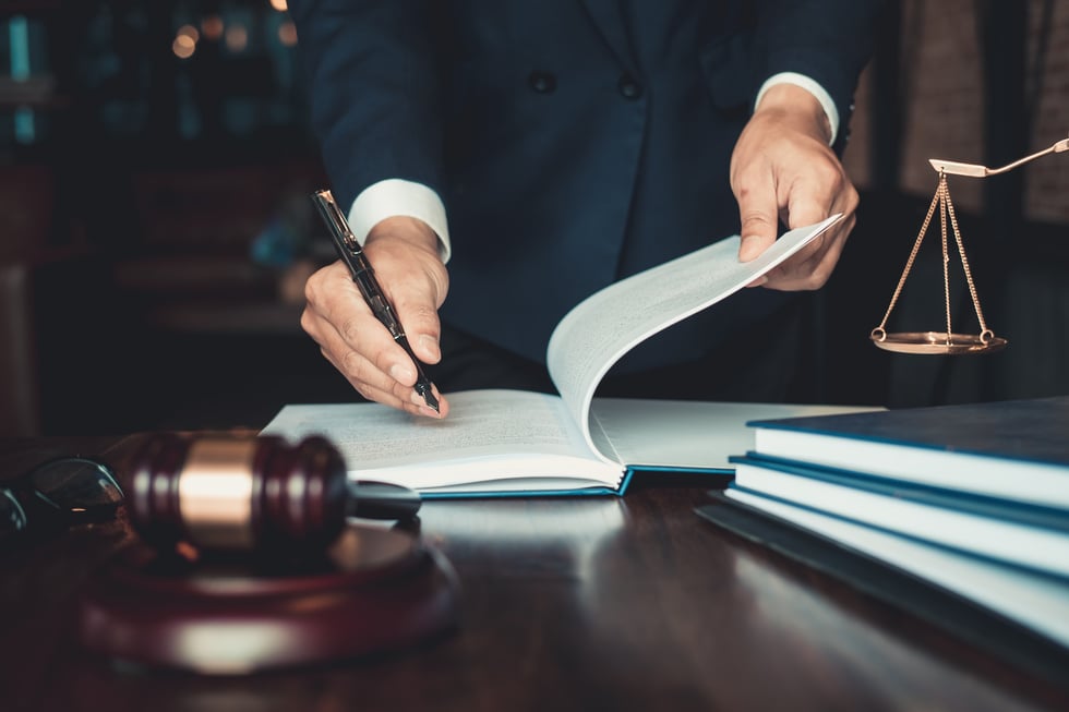 A lawyer's hand holding a pen and a book on a desk with a gavel in the background, photo for estate planning area of practice